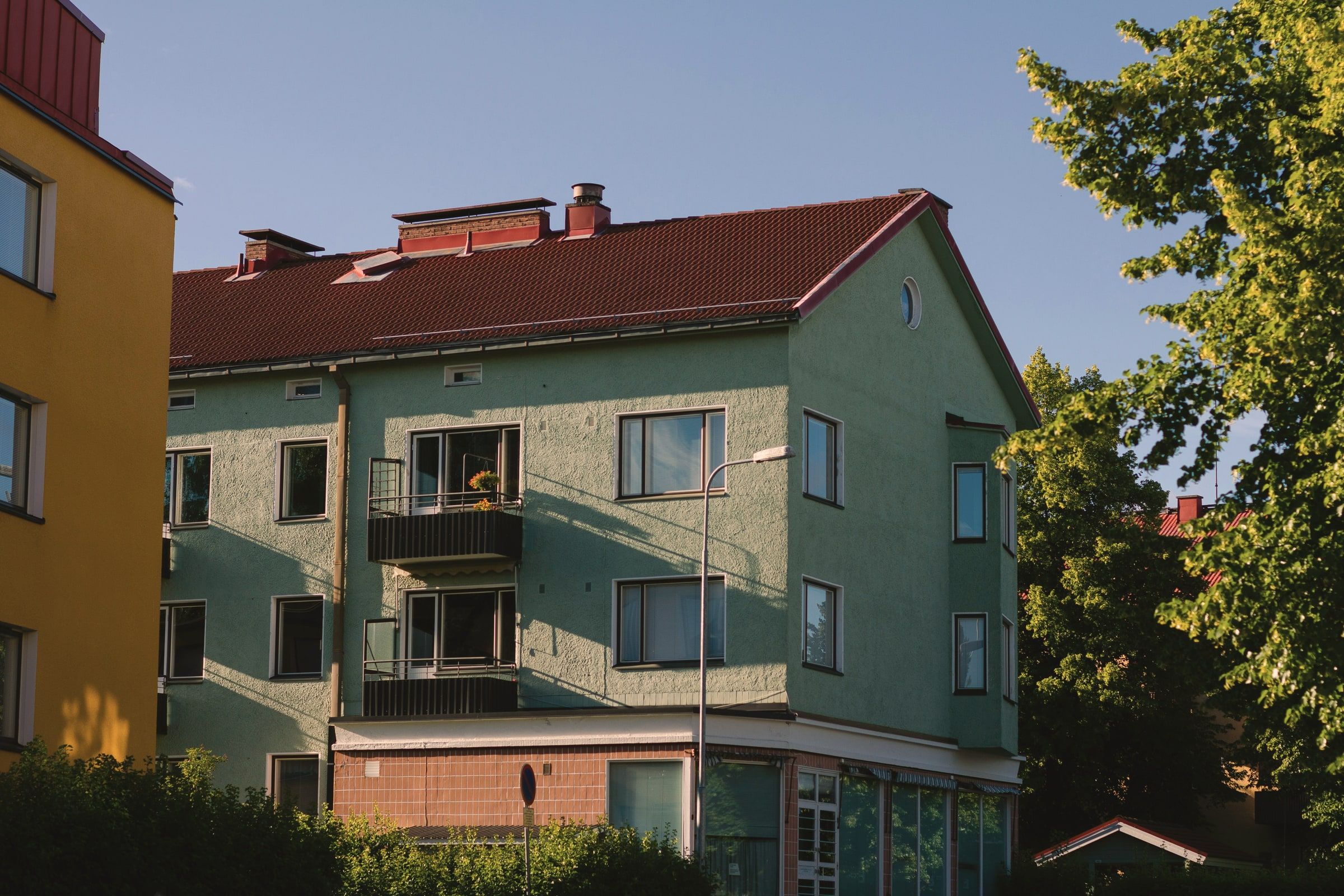 Vihreä kolmikerroksinen kerrostalo punaisella tiilikatolla kesäillan valossa